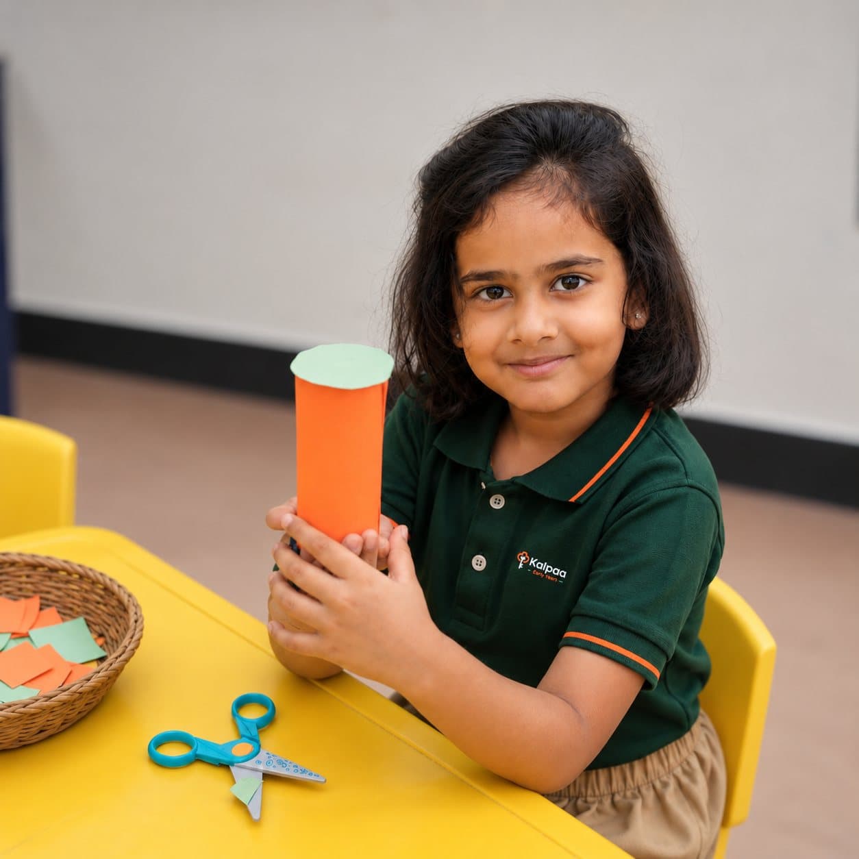 A smiling Kalpaa child holding up the paper craft she made in class