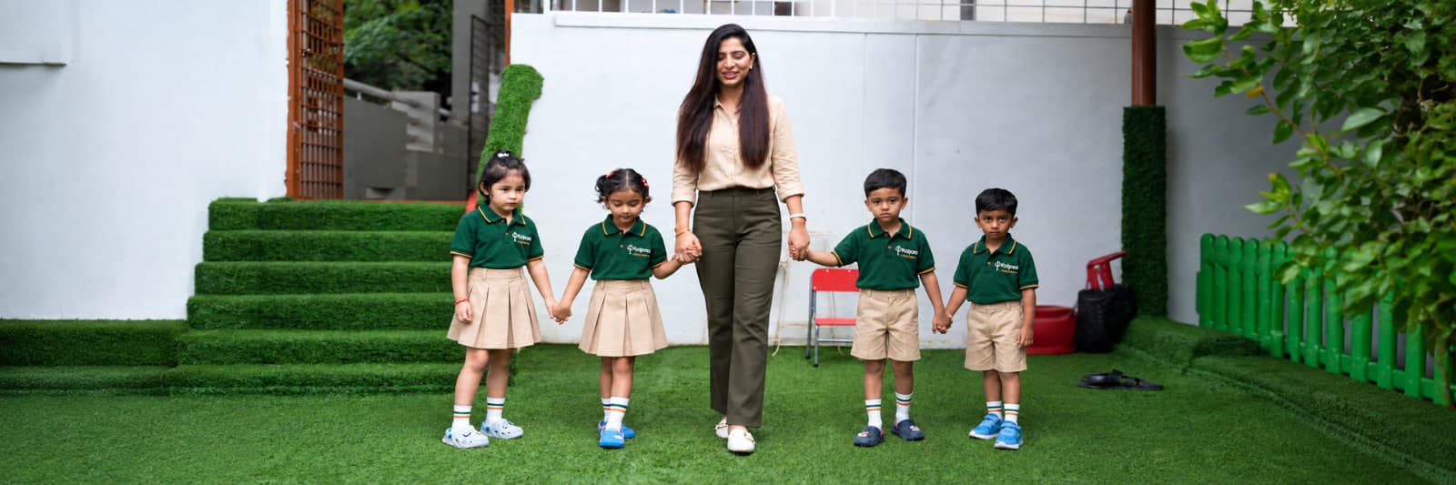 A Kalpaa teacher walking hand in hand with four children across the centre's lawn