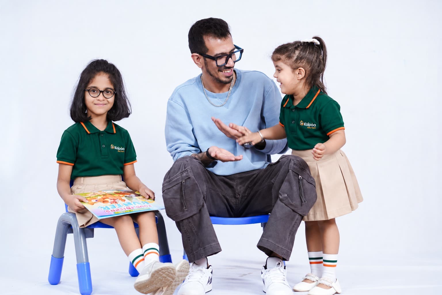 A Kalpaa teacher chatting with two girls in uniform on small classroom chairs